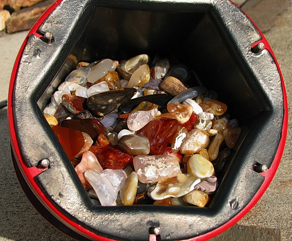 An open rotary tumbler barrel filled with agate and jasper pebbles
